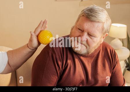 Homme âgé recevant un massage de l'épaule avec boule de thérapie spiky pour le soulagement de la douleur, le bien-être et la réhabilitation à la maison. Banque D'Images