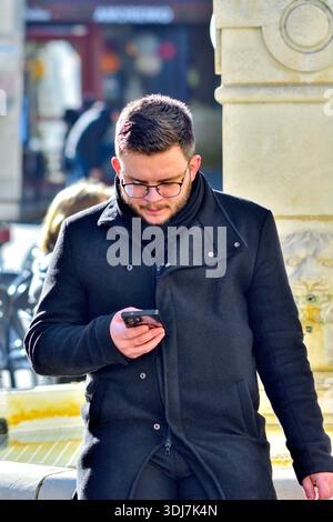 Jeune homme regardant un smartphone en marchant dans le centre-ville - Loches, Indre-et-Loire (37), France. Banque D'Images