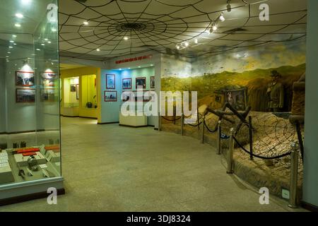 Dien bien Phu, Vietnam - 4 septembre 2022 : L'image montre une salle d'exposition à l'intérieur du musée Dien bien Phu avec un diorama de tranchée avec des mannequins, des barbelés et une murale peinte sur le champ de bataille, à côté de vitrines et de photographies historiques encadrées sur les murs. Banque D'Images