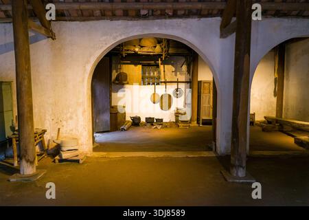 Hanoi, Vietnam - 15 septembre 2022 : L'intérieur d'une maison vietnamienne traditionnelle est exposé au Musée d'Ethnologie, montrant des piliers en bois, des portes voûtées, un sol en terre et divers outils ménagers et ustensiles accrochés au mur. Banque D'Images