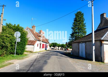 Lieu inconnu - 28 juin 2022 : une scène de rue montre des maisons traditionnelles en plâtre et en pierre avec des volets rouges, un toit en tuiles, des panneaux de signalisation, des poteaux électriques et un grand arbre sous un ciel bleu clair. Banque D'Images