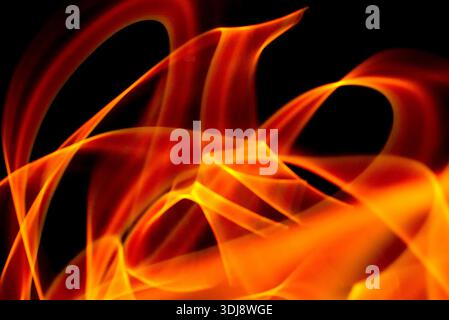 Une énergie de feu tourbillonnante puissante forme un mouvement abstrait éclatant avec des tons rouges orange vifs sur fond sombre. Banque D'Images