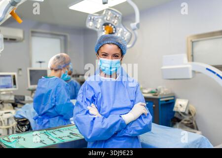 Portrait d'un chirurgien souriant à l'hôpital. Une travailleuse de la santé porte des gommages. Elle se tient debout, les bras croisés contre les lumières. Banque D'Images