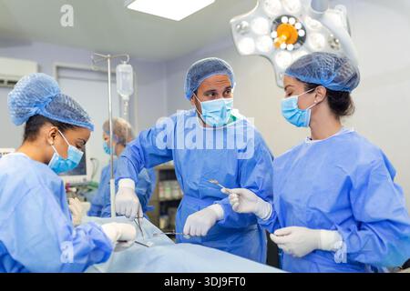 Une équipe de médecins est debout dans la salle d'urgence. Des chirurgiens multiethniques travaillent en salle d'opération à l'hôpital. Ils portent des gommages bleus. Banque D'Images