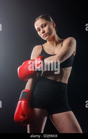 Portrait d'une femme boxeur dans des gants rouges posant dans la lumière de studio, symbolisant la confiance et la force, idéal pour les bannières de fitness, les annonces et la promotion de gymnastique Banque D'Images