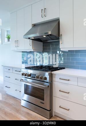 Cuisine moderne avec cuisinière à gaz en acier inoxydable, armoires blanches, dosseret en tuiles bleues et comptoirs en quartz dans un intérieur immobilier lumineux. Banque D'Images