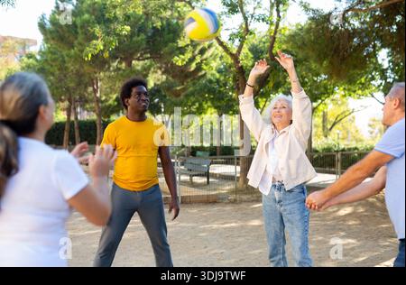 Club social de joyeux personnes âgées diverses appréciant le volley-ball le jour ensoleillé d'octobre plein air Banque D'Images