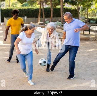 Joyeux amis multinationaux jouant au football sur un terrain de jeu sablonneux lors d'une chaude soirée de printemps Banque D'Images