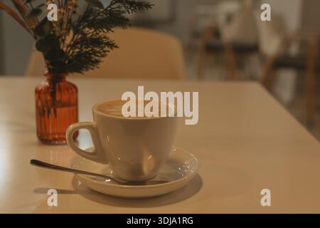 Une scène de café minimaliste avec une tasse de cappuccino servi sur une soucoupe blanche, accompagné d'un éclair garni de crème, fraises fraîches. Un petit rose Banque D'Images