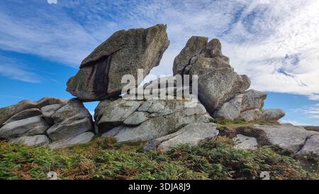 Formations rocheuses massives sous un ciel bleu avec des nuages, entourées de plantes. Banque D'Images