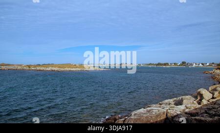 Vue sur une côte rocheuse avec un village au loin, paysage côtier alliant rivage naturel et peuplement rural. Banque D'Images