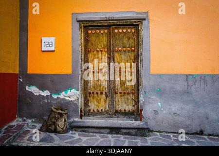 Une vieille porte en bois rustique avec des accents colorés dans un cadre mural vibrant, mettant en valeur des détails architecturaux et des textures uniques Banque D'Images