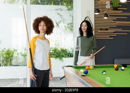 Diverses amies féminines jouant au billard dans une salle de loisirs moderne avec des repères de table en feutre vert Banque D'Images