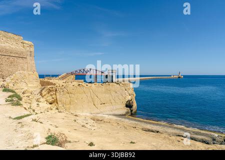 La Valette, Malte - 8 avril 2024 : vue sur le pont brise-lames historique et le phare à l'entrée du port, avec des falaises de calcaire, des fortifications Banque D'Images