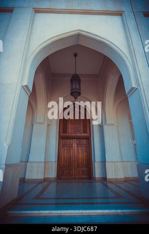 Une vue en angle bas d'une grande entrée de mosquée à Salalah, Oman, avec plusieurs structures voûtées blanches menant à un bois sombre magnifiquement sculpté Banque D'Images