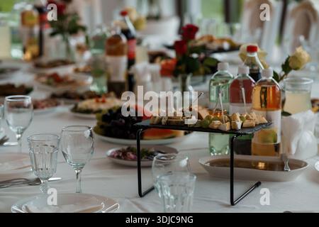 Une table de buffet magnifiquement agencée comprend un plateau de fromages gastronomiques, des raisins frais, des tranches de pastèque, des pièces maîtresses florales et des bouteilles de boisson, ide Banque D'Images