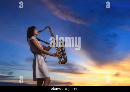 Vue latérale d'une saxophoniste se tenant devant un ciel dramatique jouant du saxophone Banque D'Images