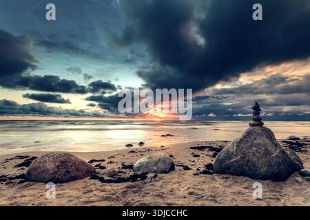 Pile de pierres sur une plage de sable au bord de la mer Baltique au coucher du soleil, Lituanie Banque D'Images