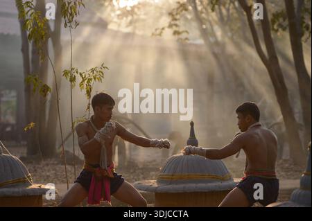 Vue de côté de deux boxeurs Muay Thai combattant à l'extérieur près d'un temple forestier au coucher du soleil, Thaïlande Banque D'Images