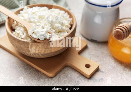 Fromage cottage servi dans un bol en bois avec une cuillère en bois, du miel et une crème Banque D'Images