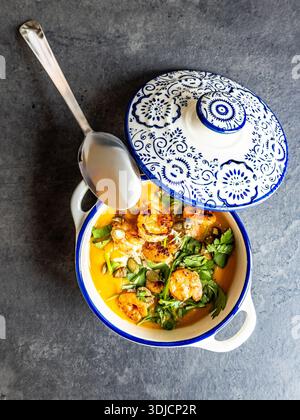 Vue aérienne de la soupe à la crème de citrouille garnie de crevettes cuites, de persil frais et de câpres, servie dans un bol décoratif en céramique bleu et blanc sur un gre Banque D'Images