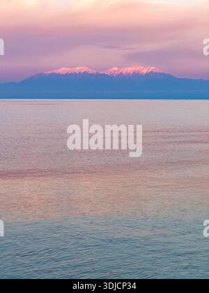 Mont Olympe vu au lever du soleil au printemps, avec des sommets enneigés illuminés par la lumière tôt le matin au-dessus des eaux calmes de la mer Égée. Banque D'Images