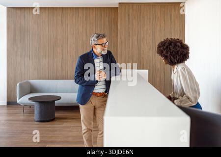 Homme d'affaires d'âge mûr discutant avec la réceptionniste de l'hôtel à la réception concernant la réservation des chambres et les services à la clientèle Banque D'Images