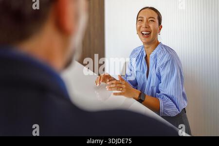 Réceptionniste joyeuse riant tout en parlant avec un homme d'affaires mature à la réception lors de l'enregistrement Banque D'Images