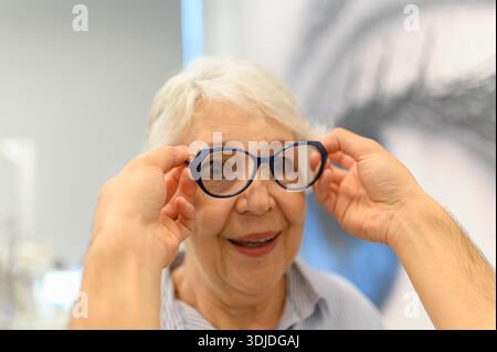 Mains de médecin recadrées portant des lunettes à la femme âgée heureuse pendant l'examen de la vue après une chirurgie oculaire réussie en clinique Banque D'Images