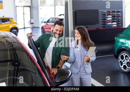 Heureux homme d'affaires d'âge moyen achetant une voiture neuve et de luxe. Belle femme dealer l'aide à prendre la bonne décision. Banque D'Images