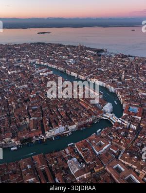 Vue aérienne des toits en terre cuite en cascade vers le Grand canal sinueux, ponctué de ponts emblématiques, Venise, Vénétie, Italie. Banque D'Images