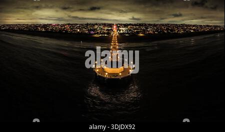 Vue aérienne de Manhattan Beach Pier s'étendant dans l'océan sombre, illuminé contre le paysage urbain sous un ciel sombre, Manhattan Beach, Californie, Banque D'Images