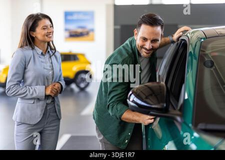 Heureux homme d'affaires d'âge moyen achetant une voiture neuve et de luxe. Belle femme dealer l'aide à prendre la bonne décision. Banque D'Images