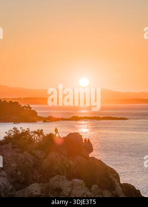 Vue aérienne de Mauao silhouettée contre le coucher de soleil ardent, projetant une lueur dorée sur les eaux tranquilles, Mont Maunganui, région de la baie de Plenty, Nouveau Banque D'Images