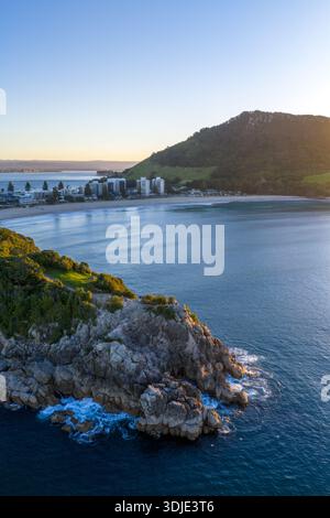 Vue aérienne de la côte rocheuse de Leisure Island rencontrant l'océan bleu profond, avec le mont Maunganui en toile de fond, le mont Maunganui, la baie de Plenty Regi Banque D'Images