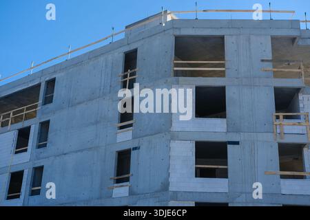 Vue à faible angle du cadre en béton gris avec remplissage en bloc blanc, baies de fenêtre ouvertes et rails de sécurité en bois ; forte lumière du soleil, ombres dures ; ciel bleu clair Banque D'Images