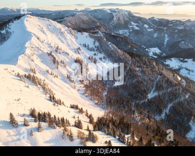 La vue aérienne des sommets enneigés et des pentes ensoleillées crée une tapisserie hivernale fascinante, Sorica, Škofja Loka, Slovénie. Banque D'Images