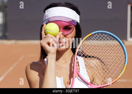 Gros plan d'une joueuse de tennis tenant une balle et une raquette sur un court de terre battue, des ombres de visière sur le visage. Idéal pour les marques de vêtements de sport, clubs de tennis, fitness a Banque D'Images