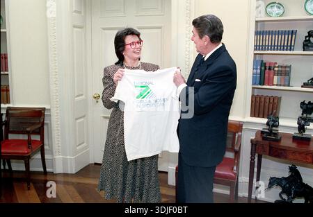 Le joueur de tennis américain Billie Jean King remet un t-shirt au président américain Ronald Reagan dans le bureau ovale de la Maison Blanche, Washington, D.C. (États-Unis), au bureau photographique du président Ronald Reagan, le 4 février 1988 Banque D'Images