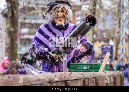 Zug, Suisse - 1er mars 2025 : interprète costumé en tenue de sorcière et masque Larve au défilé du carnaval d'hiver de Fasnacht avec un pistolet à confettis Banque D'Images