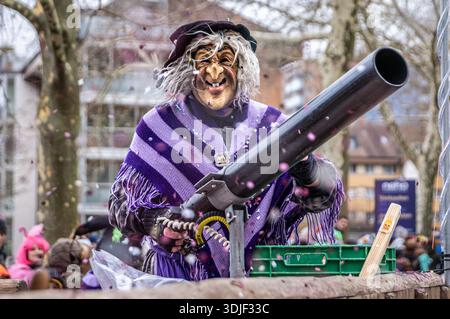 Zug, Suisse - 1er mars 2025 : interprète costumé en tenue de sorcière et masque Larve au défilé du carnaval d'hiver de Fasnacht avec un pistolet à confettis Banque D'Images