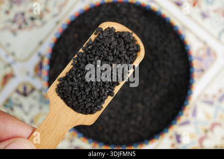 Graines de sésame de cumin noir sur une cuillère en bois au-dessus d'un bol Banque D'Images