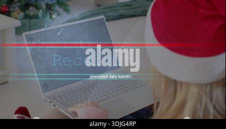 Dactylographier femme en pull rose et chapeau de Père Noël à l'aide d'un ordinateur portable argenté sur le canapé, avec arbre de Noël Banque D'Images