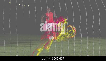 Joueur de coup de pied derrière le filet en maillot rouge blanc short frappant le terrain de nuit de ballon de football, pistes néon Banque D'Images