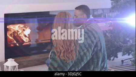 Couple câlin partageant une couverture en peluche verte et assis sur le sol du salon, près de la cheminée Banque D'Images