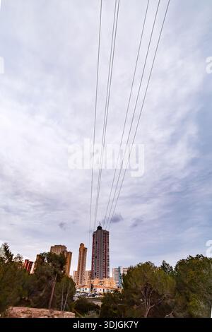 Une vue verticale grand angle regardant devant des fils électriques suspendus vers les gratte-ciel emblématiques de Benidorm, encadrés par un parc forestier verdoyant sous un Banque D'Images