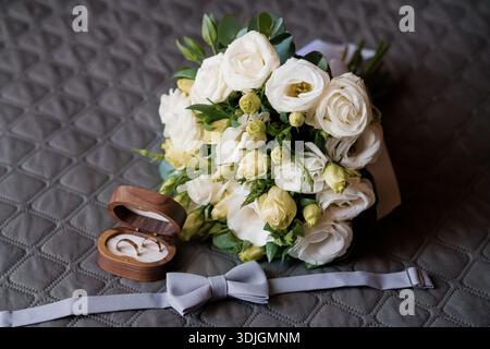 Un arrangement de mariage romantique avec un bouquet blanc luxuriant de roses et eustoma, une boîte à anneaux en bois avec des bandes de mariage en or, et un noeud papillon en argent sur Banque D'Images