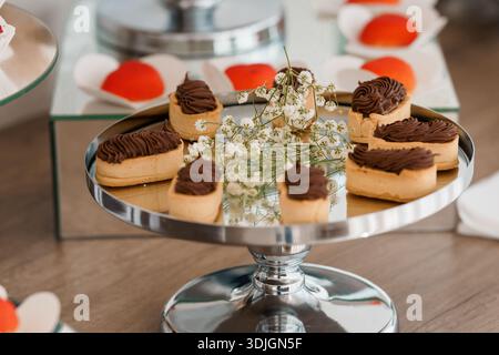 Un somptueux dessert composé de tartelettes recouvertes de chocolat sur un présentoir à gâteaux argentés en miroir, garni de fleurs de souffle et d'entouillement rouge de bébé Banque D'Images