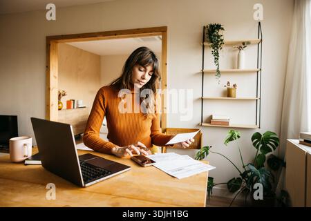 Femme gérant les factures et les finances au bureau à domicile en utilisant un ordinateur portable Banque D'Images