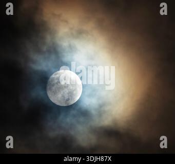 Nuages brillants orange et bleu avec la lune brillante pleine et brillante derrière. Banque D'Images